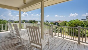 A wooden deck with white chairs and a white railing, overlooking a residential area and the ocean. - Point of View: Saltwater Pool, Hot Tub, Amazing Ocean and Sound Views (Duck)