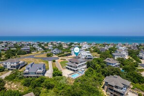 Vista aérea de uma área residencial à beira-mar, com casas, piscina e um marcador azul que destaca um ponto de interesse.