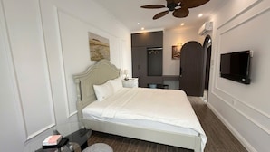 Una habitación de hotel moderna con una cama grande, un ventilador de techo, un televisor de pantalla plana y un pequeño rincón de descanso.