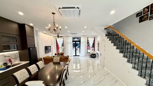 Un comedor amplio con una mesa larga y sillas, una cocina con electrodomésticos modernos, y una escalera que sube a un nivel superior.