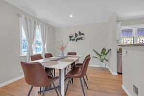 Uma área de refeições com uma mesa retangular, seis cadeiras marrons e um vaso com flores.