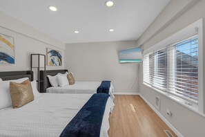 Quarto de hotel com duas camas, uma janela grande com cortinas, televisão de tela plana na parede e obras de arte nas paredes.