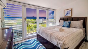 Un dormitorio con una cama grande, vistas al exterior a través de un ventanal corredera y un ventilador de techo.