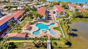 Vista aérea de un resort con una piscina central, rodeado de edificios y palmeras.