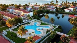 Un resort con una piscina central, rodeado de palmeras y vistas al océano.
