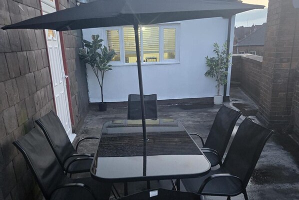 A patio with a table and chairs, a black umbrella, and potted plants. - 2 Bed - Sleeps 6 - Private Balcony - City Centre (Wolverhampton)