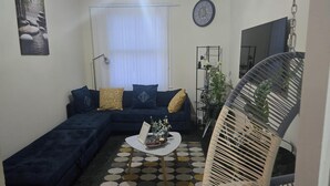 A living room with a dark blue sectional sofa, a round coffee table, a patterned rug, a wall clock, and a ceiling light fixture. - 2 Bed - Sleeps 6 - Private Balcony - City Centre (Wolverhampton)
