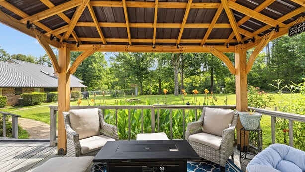 A covered outdoor seating area with wicker furniture and a black table, overlooking a well-maintained garden and a golf course. - Charming Guest House – 1BR + Sleeping Nook, Full Kitchen, Gazebo, & Boat Parking (Marshall)
