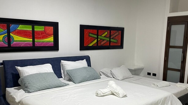 A double bed with white and blue bedding, two pillows, and a rolled towel on a blue headboard. There are two abstract paintings on the wall. - Apartment 201 (San Andrés Islas)