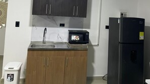 A compact kitchen with dark cabinets, a microwave, a refrigerator, and a trash bin. - Apartment 201 (San Andrés Islas)