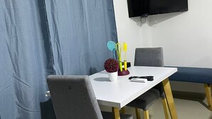 A modern dining area with a white table, grey chairs, and a blue curtain. A flat-screen TV is mounted on the wall. - Apartment 201 (San Andrés Islas)