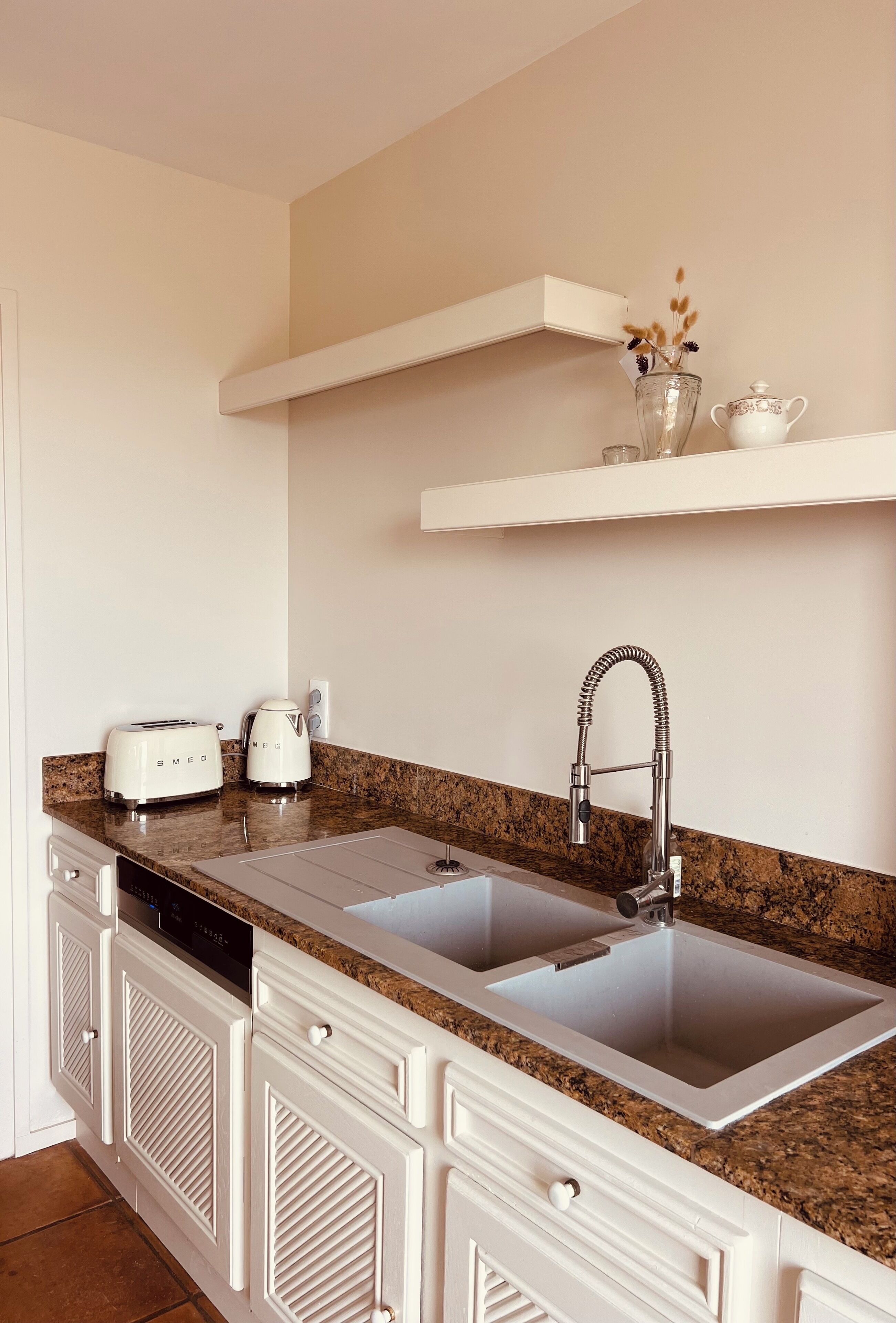 Una cocina con un lavamanos doble, muebles blancos, lavavajillas integrado y un grifo de acero inoxidable.