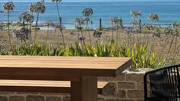 Une table et des chaises en bois, placées de manière à offrir une vue sur la plage et l’océan.