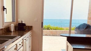 Une cuisine moderne dotée d’une grande fenêtre et d’une porte-fenêtre coulissante donnant sur une terrasse avec vue sur la mer.