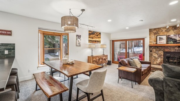 Amplia sala de estar con una mesa de comedor de madera, asientos cómodos, una chimenea de piedra y grandes ventanas que ofrecen vistas al exterior.
