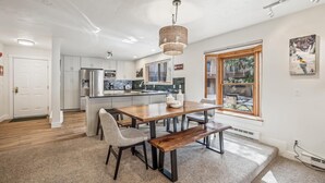 Una cocina moderna con armarios blancos, electrodomésticos de acero inoxidable y una mesa de comedor de madera con bancos.