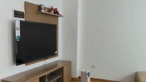 Un soggiorno moderno con una TV a schermo piatto montata su un mobile in legno, un termosifone e un piccolo tappeto sul pavimento in legno.