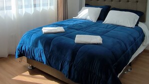 A modern bedroom with a large bed, a headboard, and a window with curtains.