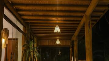 An outdoor wooden deck with a pool, wooden furniture, and hanging lights.