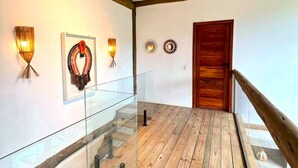 Un pasillo con suelo de madera, barandillas de vidrio y apliques de luz en la pared.