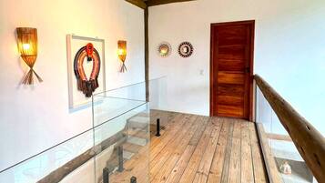 Un pasillo con suelo de madera, barandillas de vidrio y apliques de luz en la pared.
