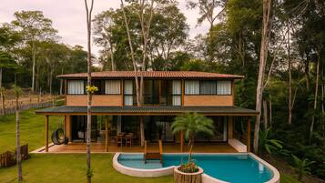Una casa de dos pisos con piscina, rodeada de árboles.