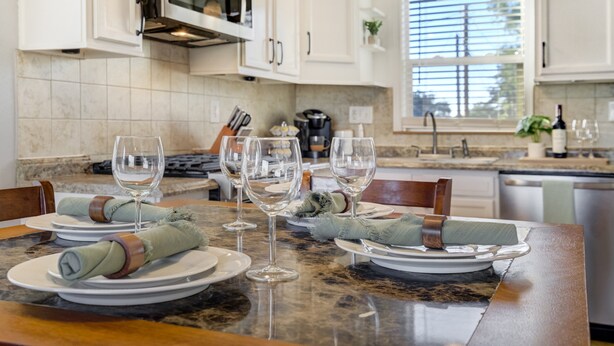 A modern kitchen with white cabinets, a granite countertop, and a dining area set with plates, glasses, and a knife block. - Charming 2BR Retreat | Pet Friendly! (Colorado Springs)