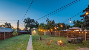 A backyard with a wooden fence, a small tree, a fire pit, and string lights. - Charming 2BR Retreat | Pet Friendly! (Colorado Springs)