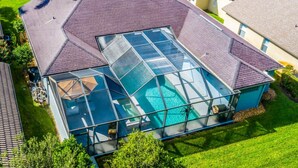 Una casa moderna con una gran piscina cubierta por vidrio, techo inclinado y césped bien cuidado.