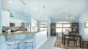 Una cocina amplia con una isla central, taburetes de bar, una zona de comedor con mesa y sillas, y una estantería.
