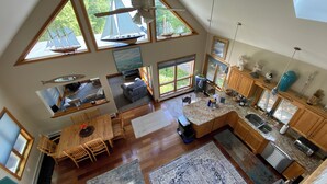 Un vaste espace de vie aménagé dans un style loft, avec un plafond haut, de grandes fenêtres et une cuisine dotée d’armoires en bois et de plans de travail en granit.