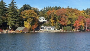 Une propriété au bord du lac, comprenant une maison principale et un petit chalet, le tout entouré d’arbres aux couleurs automnales.