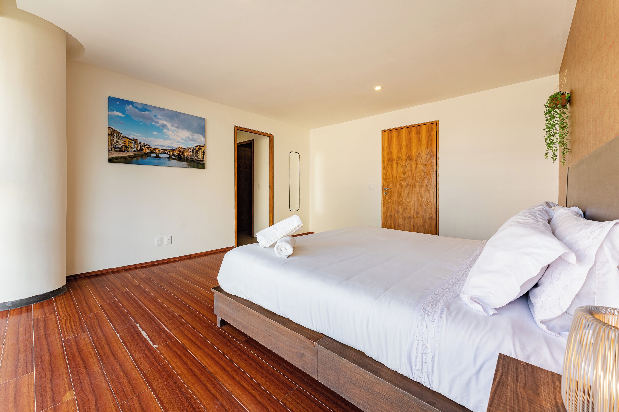 Ein modernes Schlafzimmer mit einem großen Bett, Holzboden, einem Stadtbildgemälde und einer Holztür.