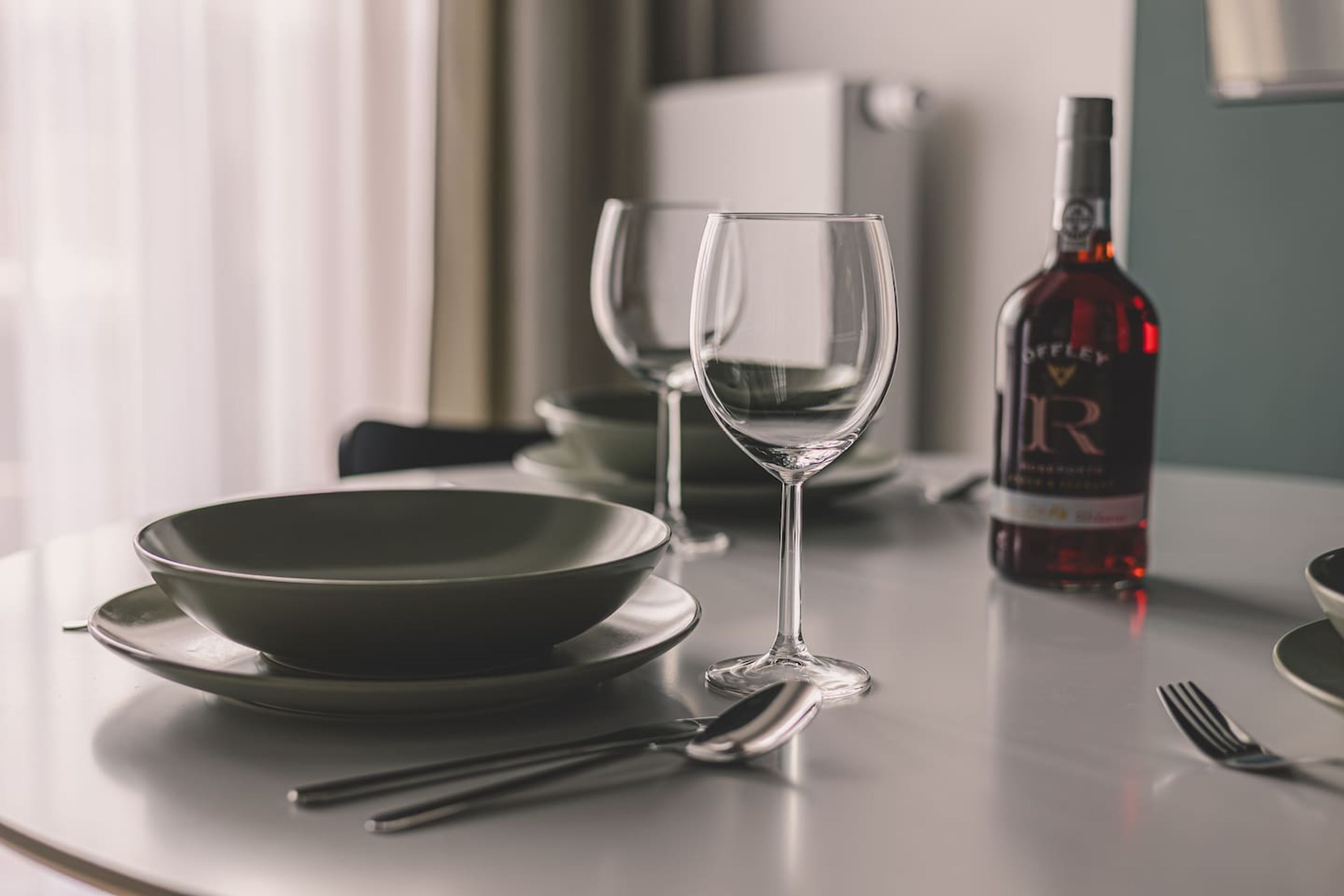Una mesa de comedor con una botella de vino, dos copas de vino y cubiertos.