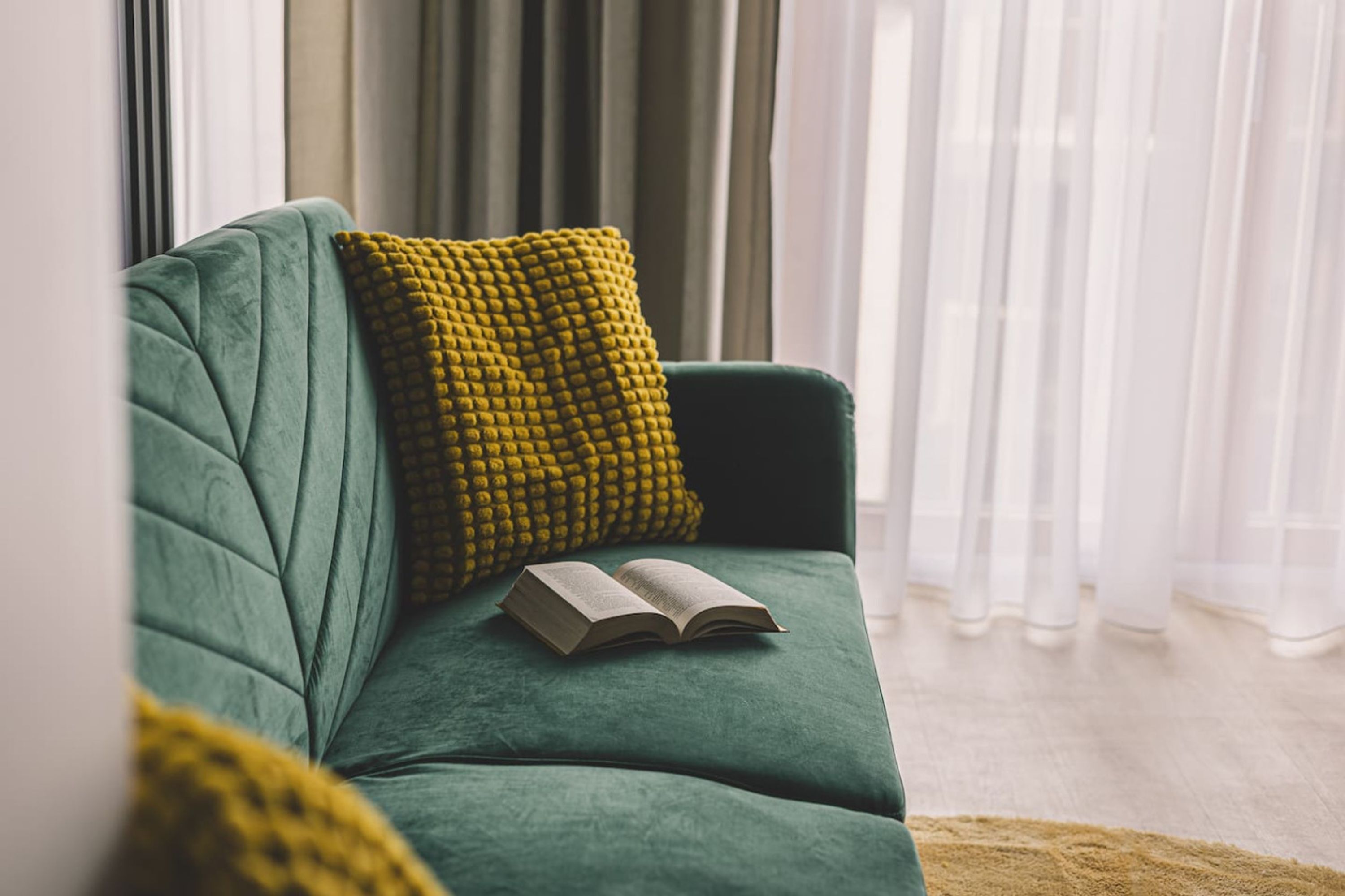 Un sofá verde con un cojín amarillo y un libro abierto.