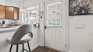 A modern kitchen with white cabinetry, a grey bar stool, a pendant light, and a cityscape framed on the wall. - Spacious 1-Bedroom Apartment in the Heart of Indy (Indianapolis)
