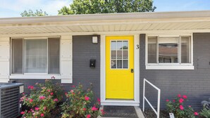 A building with a bright yellow door, numbered 3, and a small porch area with pink flowers. - Spacious 1-Bedroom Apartment in the Heart of Indy (Indianapolis)