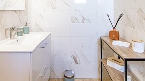 Un baño moderno con paredes de mármol, un lavabo blanco y un estante de madera con un difusor.