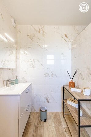 A modern bathroom with marble walls, a white sink, and a wooden shelf with a diffuser. - Chez Jean - BOIS SAINTE MARIE (BOIS SAINTE MARIE)