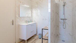 Un baño moderno con un tocador blanco, un espejo, ducha con cabezal de ducha manual y paredes con diseño de mármol.