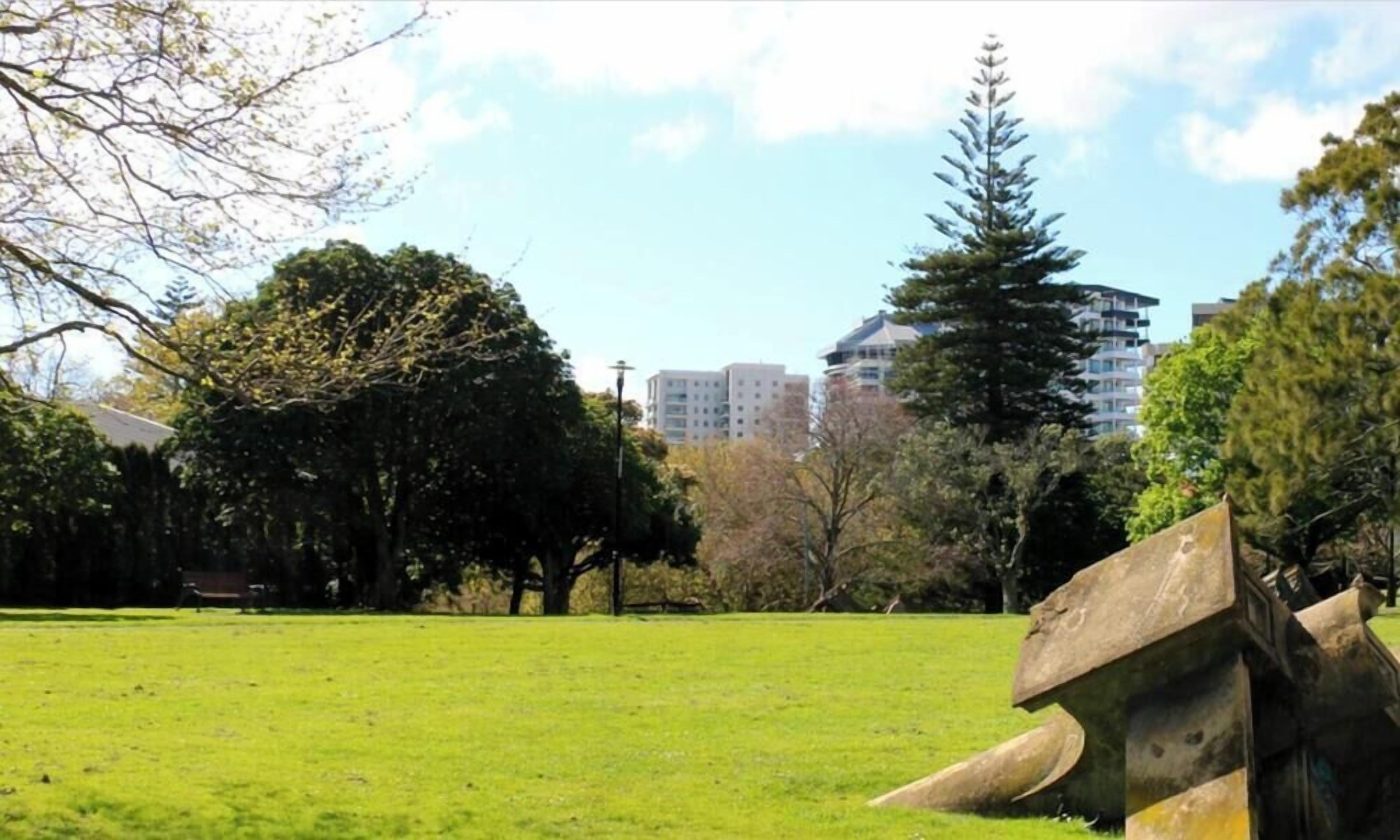 A park with a grassy field, trees, and buildings in the background.