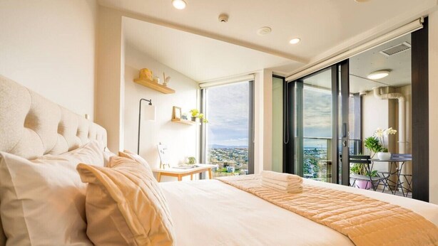 A bedroom with a large bed, a desk, and a view through a sliding glass door. - Cosy 2 Bedroom Apartment with City Conveniences (Auckland)