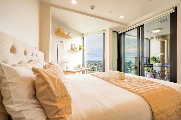 Un dormitorio con una cama grande, un escritorio y vistas a través de un ventanal corredera.