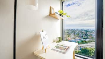 Ein Büro im Eck mit weißem Schreibtisch, einer Tafel, einer kleinen Pflanze und Blick auf eine Stadtkulisse durch ein großes Fenster.