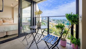 A balcony with a bed, a table, chairs, and potted plants. - Cosy 2 Bedroom Apartment with City Conveniences (Auckland)
