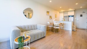 A modern living room with a sofa, dining table, and chairs, a kitchen area with cabinets and a refrigerator, and a large mirror on the wall. - Cosy 2 Bedroom Apartment with City Conveniences (Auckland)