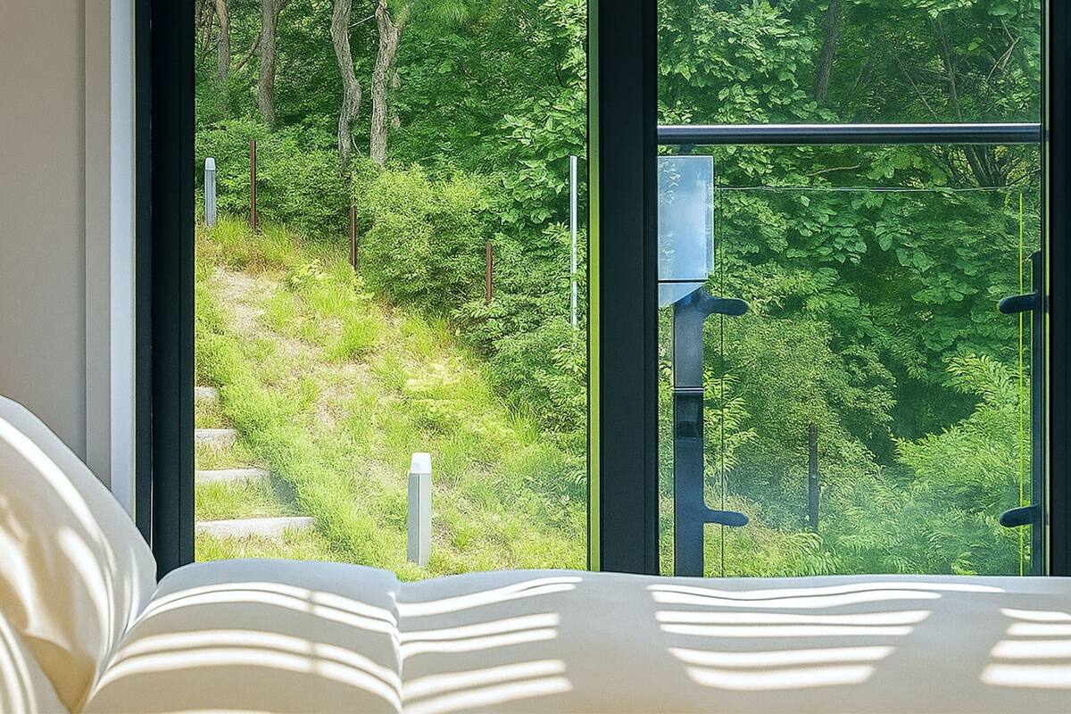 A bedroom with a large window overlooking a forested hillside.