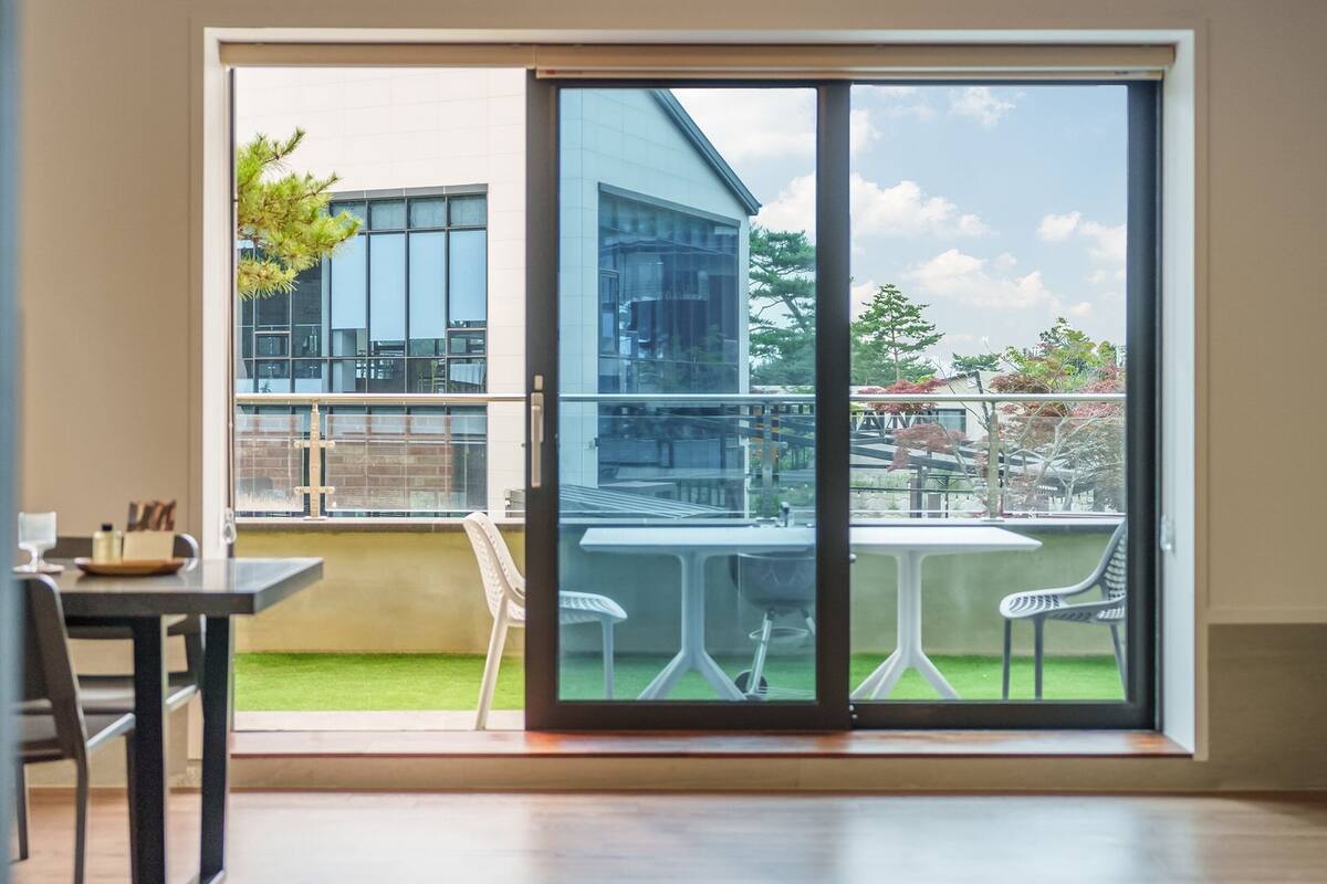 A modern room with a sliding glass door leading to a balcony with a view of buildings and trees.