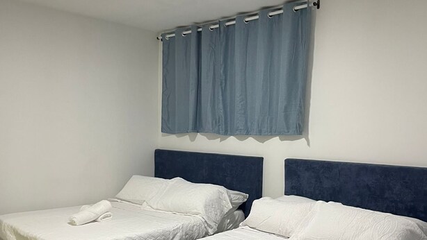 A room with two beds, each with a blue headboard, white bedding, and a rolled towel on the bed. - Apartment 202A (San Andrés Islas)