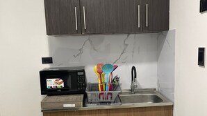 A compact kitchen with dark wooden cabinets, a microwave, a sink, and a trash bin. - Apartment 202A (San Andrés Islas)